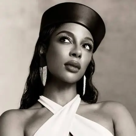 Victoria Monét poses in a sepia-toned portrait wearing a leather cap and draped white halter top