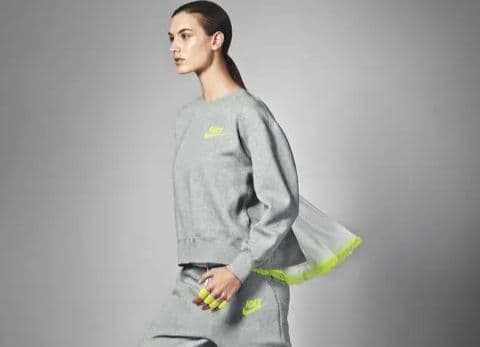 Model wearing NikeLab x sacai heather grey Tech Fleece sweatshirt featuring signature billowing pleated back panel with neon volt trim in motion.