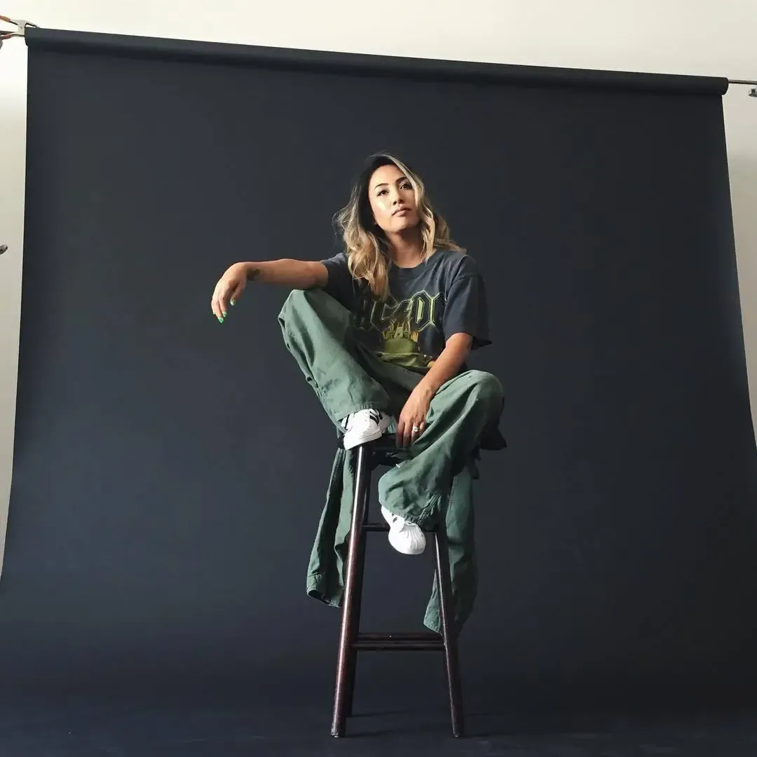 Miss Lawn, founder of HLZBLZ, seated on a stool in a studio portrait wearing a graphic tee and green cargo pants
